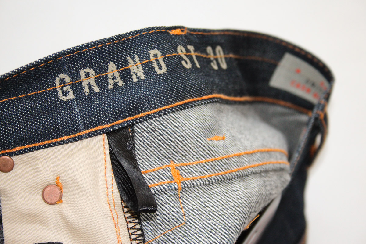 waistband of Grand St. raw denim jeans with orange stitch details
